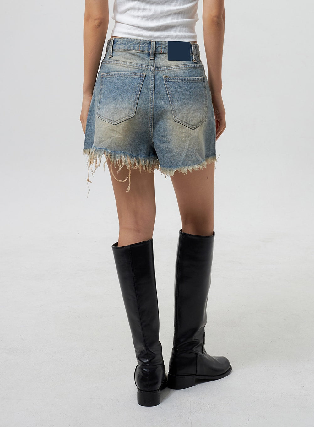 Mid-Rise Ripped Jeans CY323 in light blue, back view on model, dual back pockets with navy label patch, raw frayed hem and vintage wash visible from behind, styled with knee boots.
