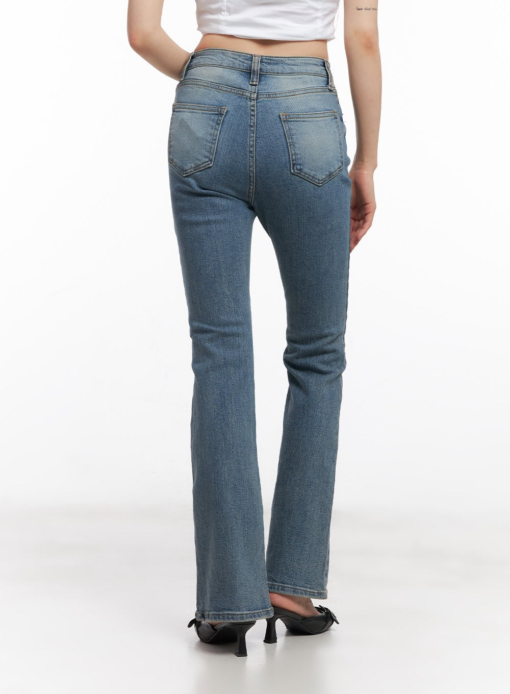 Cassy Slim Washed Flared Jeans CY512 in blue, back close-up from waist to hem on model, featuring back patch pockets and gentle flare with washed denim texture, white crop top.