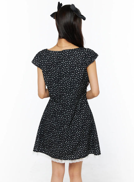 Floral Lace Trim Mini Dress CU522 in black, close back view on model, back neckline, cap flutter sleeves, fitted waist, flared skirt with white lace trim at hem.