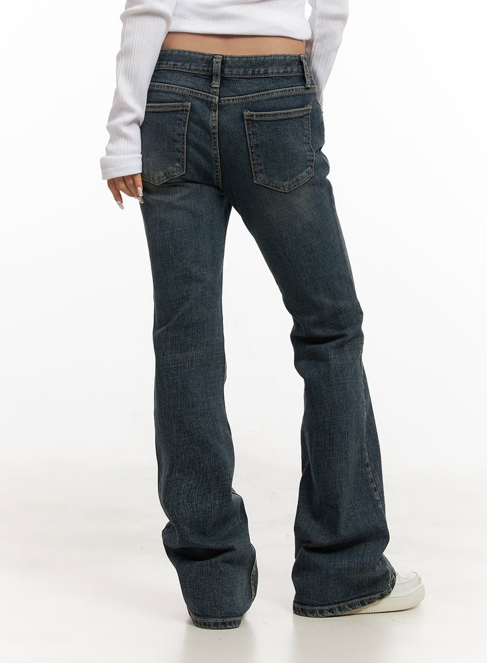Natalia Low-Rise Flared Jeans CJ508 in dark blue, back close-up on model, low-rise waistband and dual back pockets with contrast stitching, washed bootcut flare hem, worn with white ribbed top.