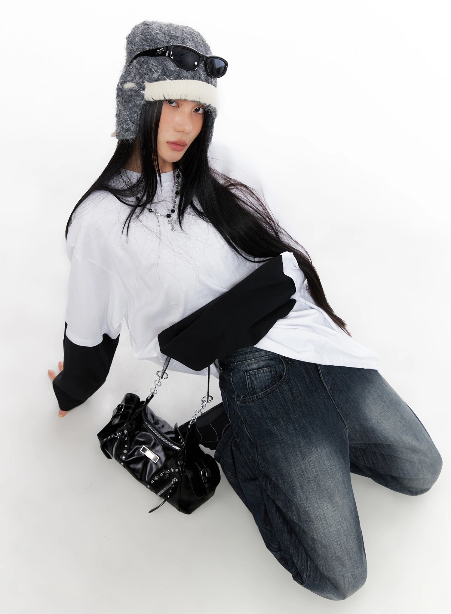 Minnell Vintage-Wash Wide-Leg Jeans IO517 in dark blue, overhead angle model kneeling, styled with white layered tee, trapper hat, sunglasses, and black studded mini bag, acubi street look.