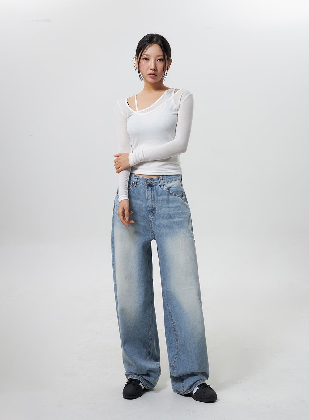 Low Rise Baggy Jeans CY324 in light blue, full-length front view on model with arms crossed, low-rise wide-leg faded denim, styled with white asymmetric cutout long-sleeve top and sneakers.