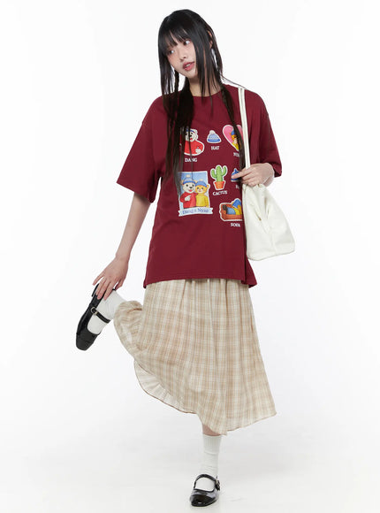 Oversized Graphic Print Tee CU519 in dark red, full-length front view on model in playful pose, Dang & Nyao graphic tee styled with beige plaid skirt, white socks, and white shoulder bag.