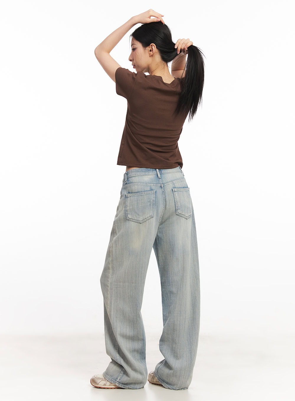 Jessi Washed Wide-Leg Jeans CA514 in light blue, back full-body shot on model tying hair up, rear patch pockets and low-rise waist visible, styled with brown crop tee.