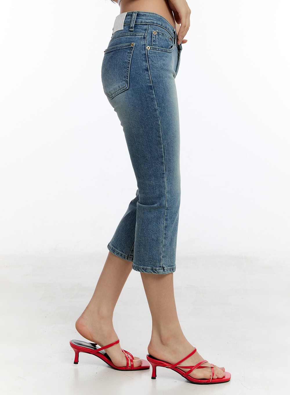 Kyra Cropped Low-Rise Skinny Jeans IU503 in blue, side view on model, washed denim showing low-rise silhouette, back pocket detail and slight flare at cropped hem, paired with red heeled mules.