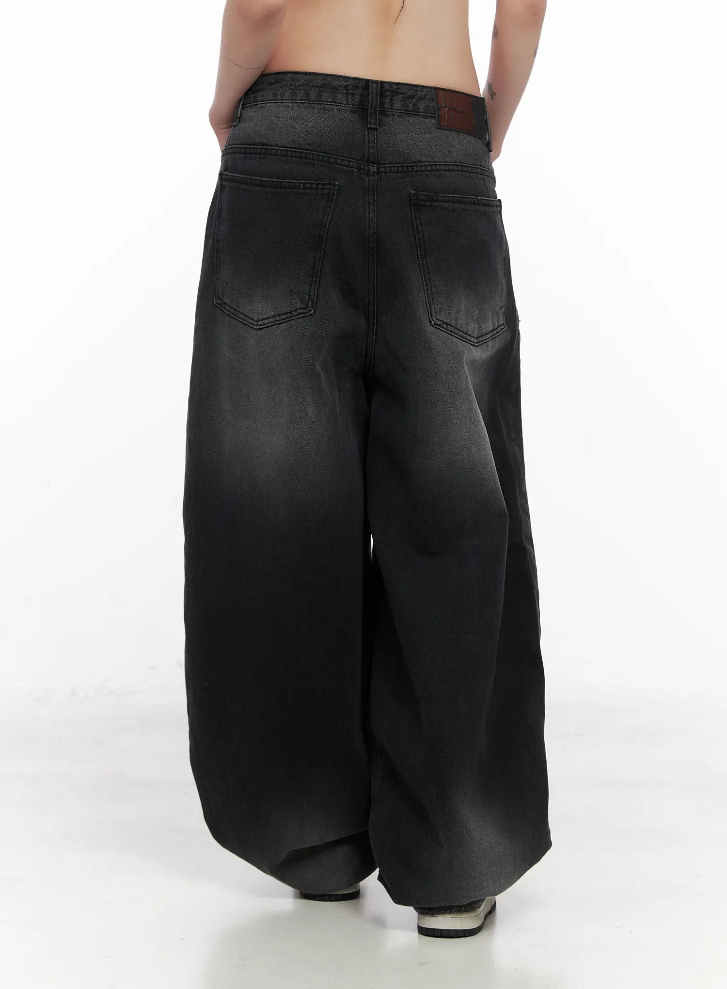 Yuji Dark-Washed Baggy Jeans CN513 in black, back close-up from waist to hem on model, featuring back patch pockets, brown leather brand tab at waistband, and dark-to-faded wash cotton denim.
