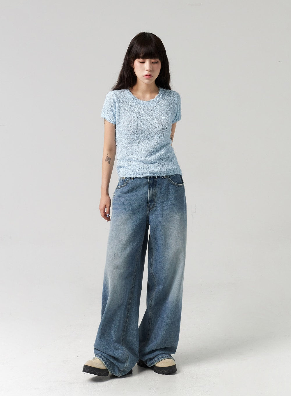 Baggy Jeans CL313 in washed blue, full-length front view on model looking down, relaxed wide-leg silhouette with faded wash pooling at hem, styled with blue bouclé top.