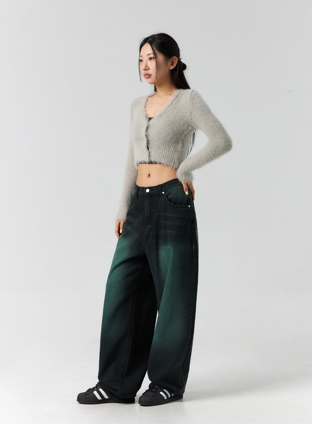 Comfy Wide Leg Color Jeans CS305 in dark green, three-quarter side view on model looking away, wide-fit cotton denim with dark green gradient wash, styled with grey crop cardigan and sneakers.