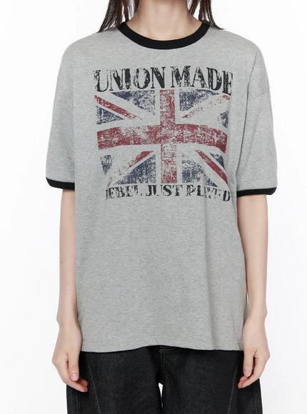 Graphic Short Sleeve Tee CU519 in gray, torso close-up on model, showing distressed Union Jack print with UNION MADE and REBEL JUST PLAYED text, black ringer collar detail.