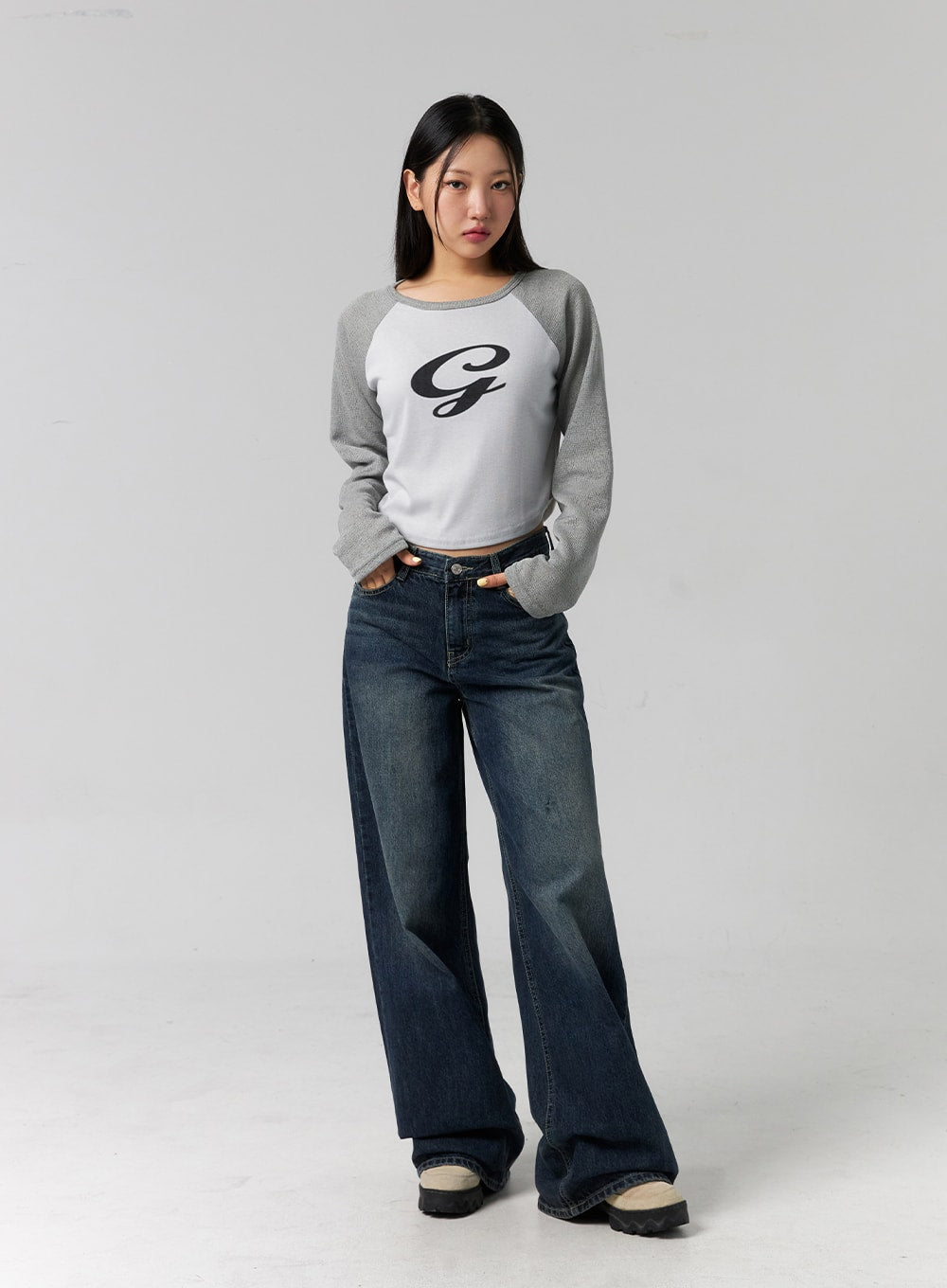 Low Rise Washed Wide Jeans CG315 in dark blue, full-body front shot on model with hands in pockets, low-rise waist, relaxed wide-leg silhouette, paired with grey raglan crop top.