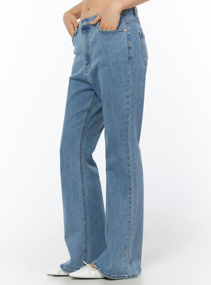 Leana Stretch Bootcut Jeans IU519 in blue, side view on model hand in pocket, elongated bootcut flare line, visible front-seam detail, washed stretch denim, white flats.