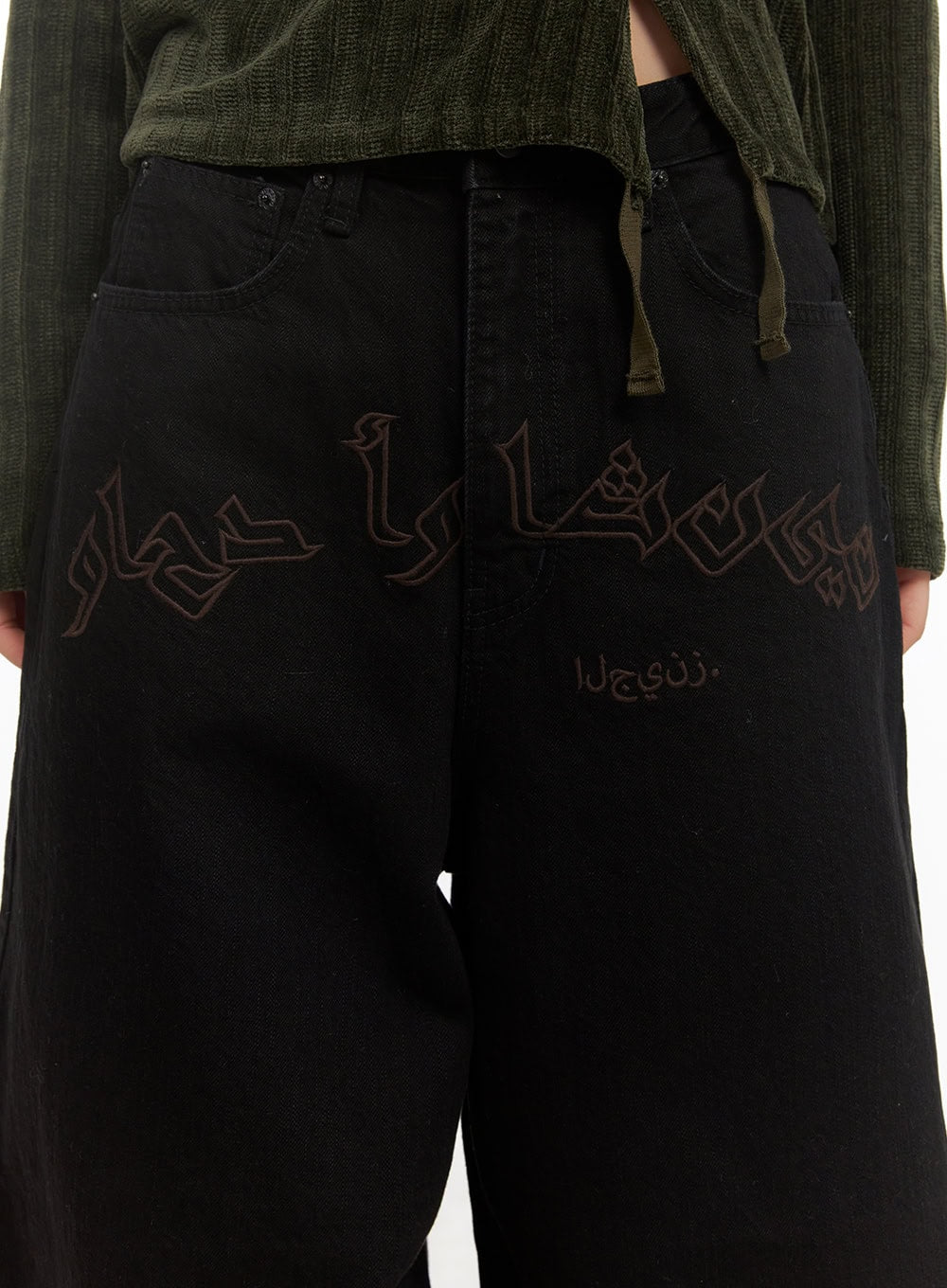 Yasmin Denim Wide Fit Jeans CD413 in black, front detail close-up on model, large-scale tone-on-tone Arabic-style lettering embroidery across hip panel, heavy cotton denim texture visible.