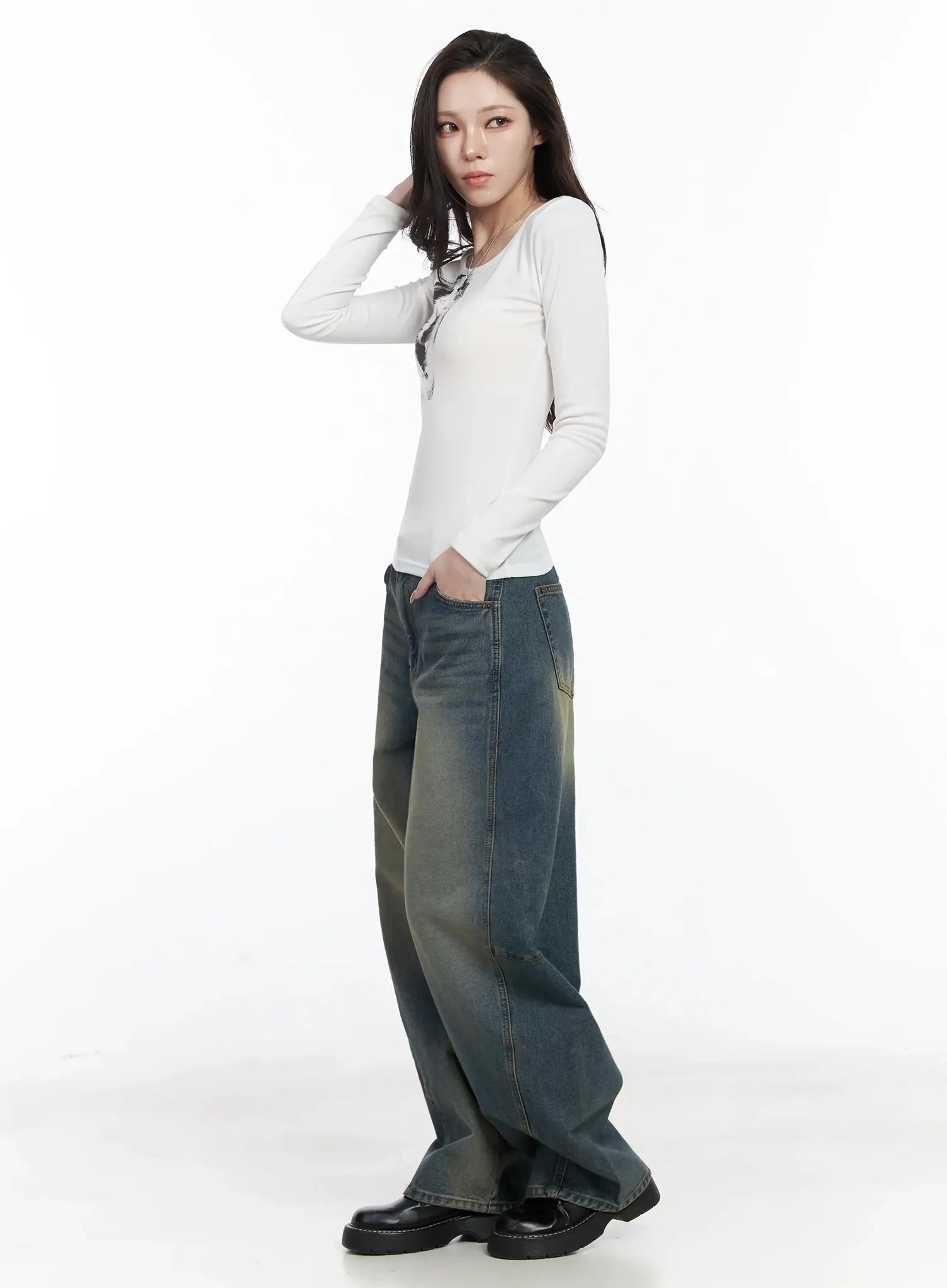 Tata Vintage Dark Blue Washed Wide Leg Jeans IJ528 in dark blue, side-angled full-body shot on model, hand in hair, wide leg silhouette with yellow-tinted wash showing on side panels, styled with white fitted long-sleeve top.