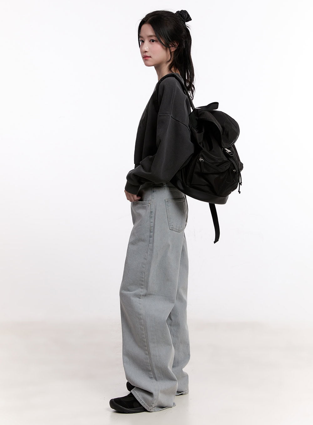 Casey Washed Baggy Wide-Leg Jeans CM526 in light gray, side full-body shot on model glancing back, wide-leg washed denim with hand in pocket, styled with oversized dark sweatshirt and backpack.