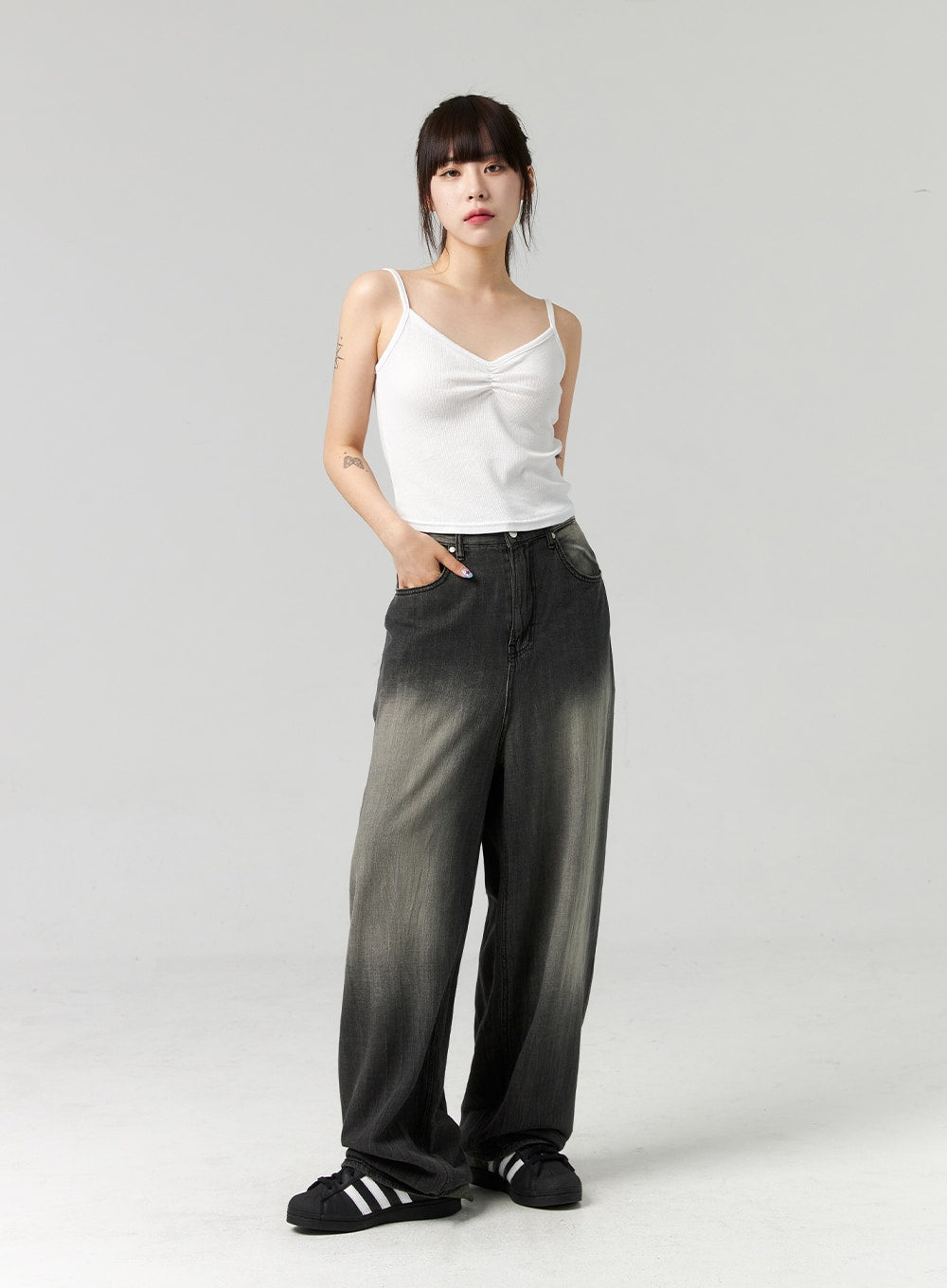 Baggy Jeans CL321 in washed dark grey, full-body front view on model, wide-leg washed denim with grey-to-dark gradient, hand in pocket, styled with white cami top and black sneakers.