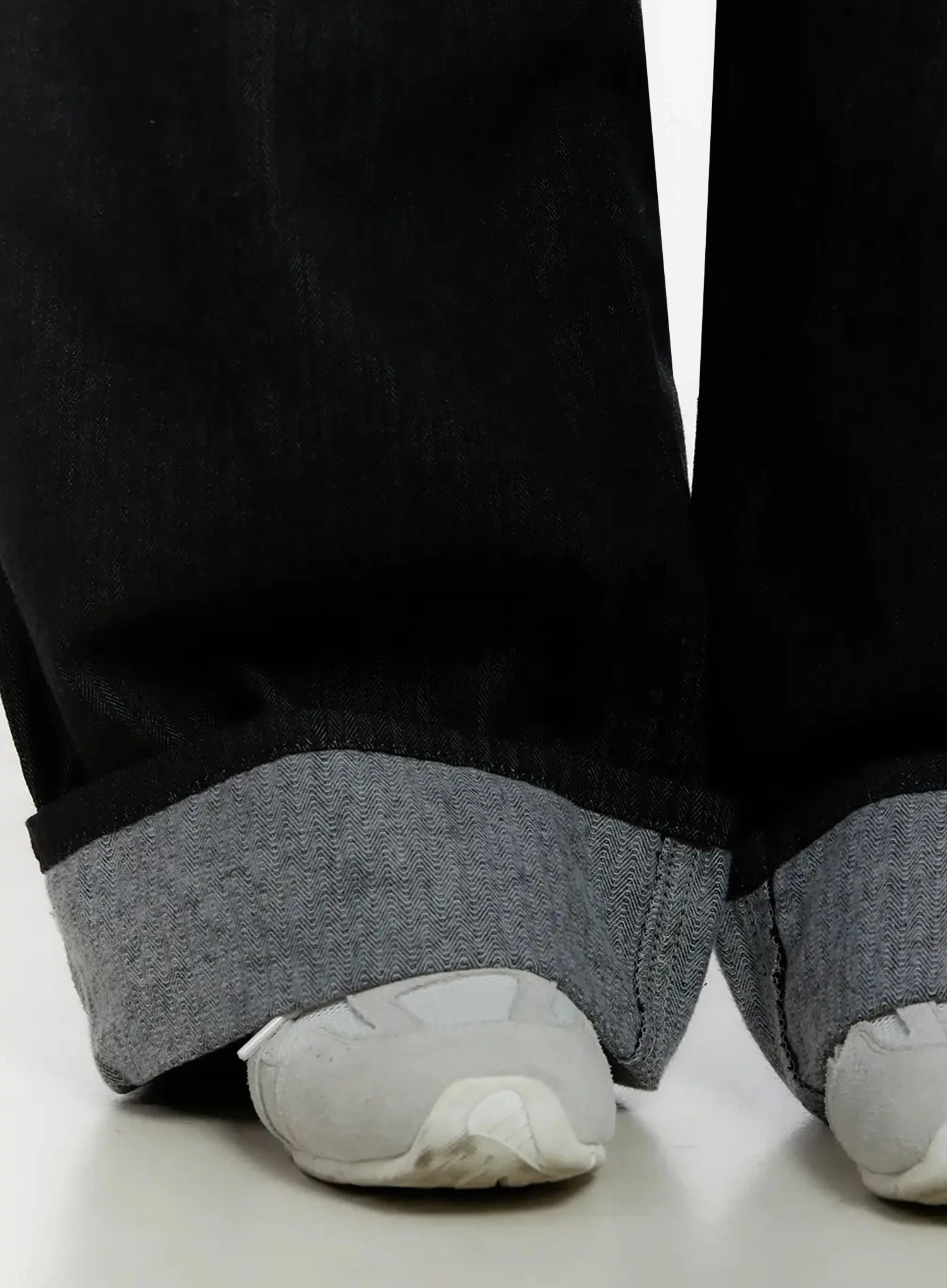Amyra Baggy Striped Jeans ID525 in black, close-up detail of cuffed hem on model, contrast grey rolled cuff with visible herringbone-stripe denim reverse, white sneakers beneath.