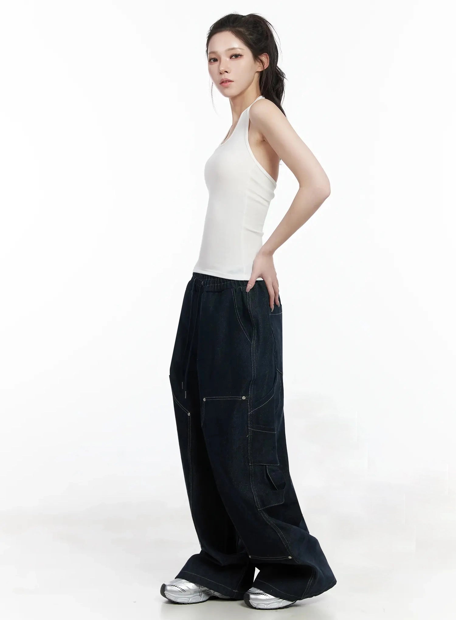 Ashlyn Carpenter Wide-Leg Jeans IJ528 in dark blue, side view on model in white halter top, oversized wide-leg drape with curved cargo pockets and contrast topstitching, floor-grazing length.
