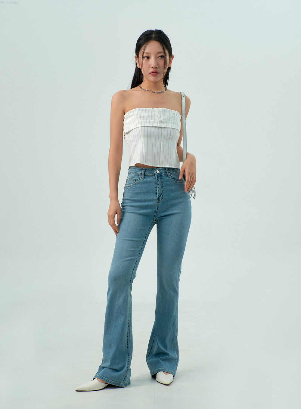 Light Wash Bootcut Jeans CY330 in light blue, full front view on model with shoulder bag, high-rise washed denim bootcut, slim silhouette with flared hem, styled with white strapless crop top.