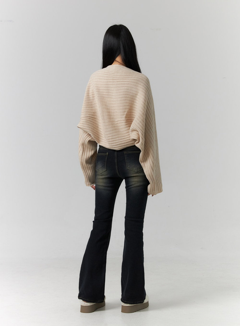 Washed Low Rise Bootcut Jeans CD308 in dark blue, full back view on model, rear patch pockets with contrast stitching, slim fit through hips with bootcut flare, paired with beige ribbed cardigan.