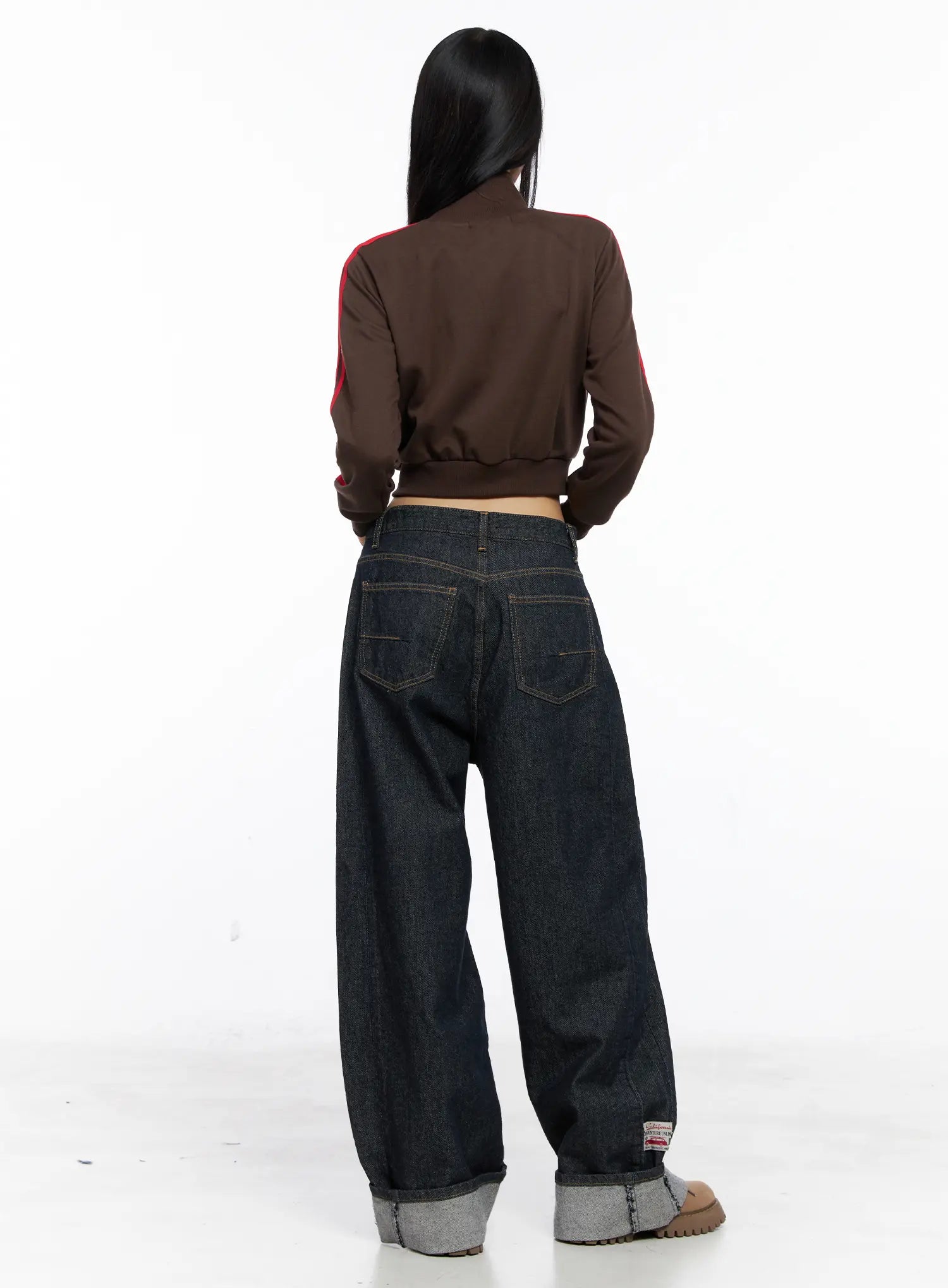 Oakley Cuffed Wide-Leg Jeans CS511 in dark blue, back full-length styled shot on model, wide baggy silhouette with back pockets, grey cuffed hem, woven patch label, with brown crop jacket.