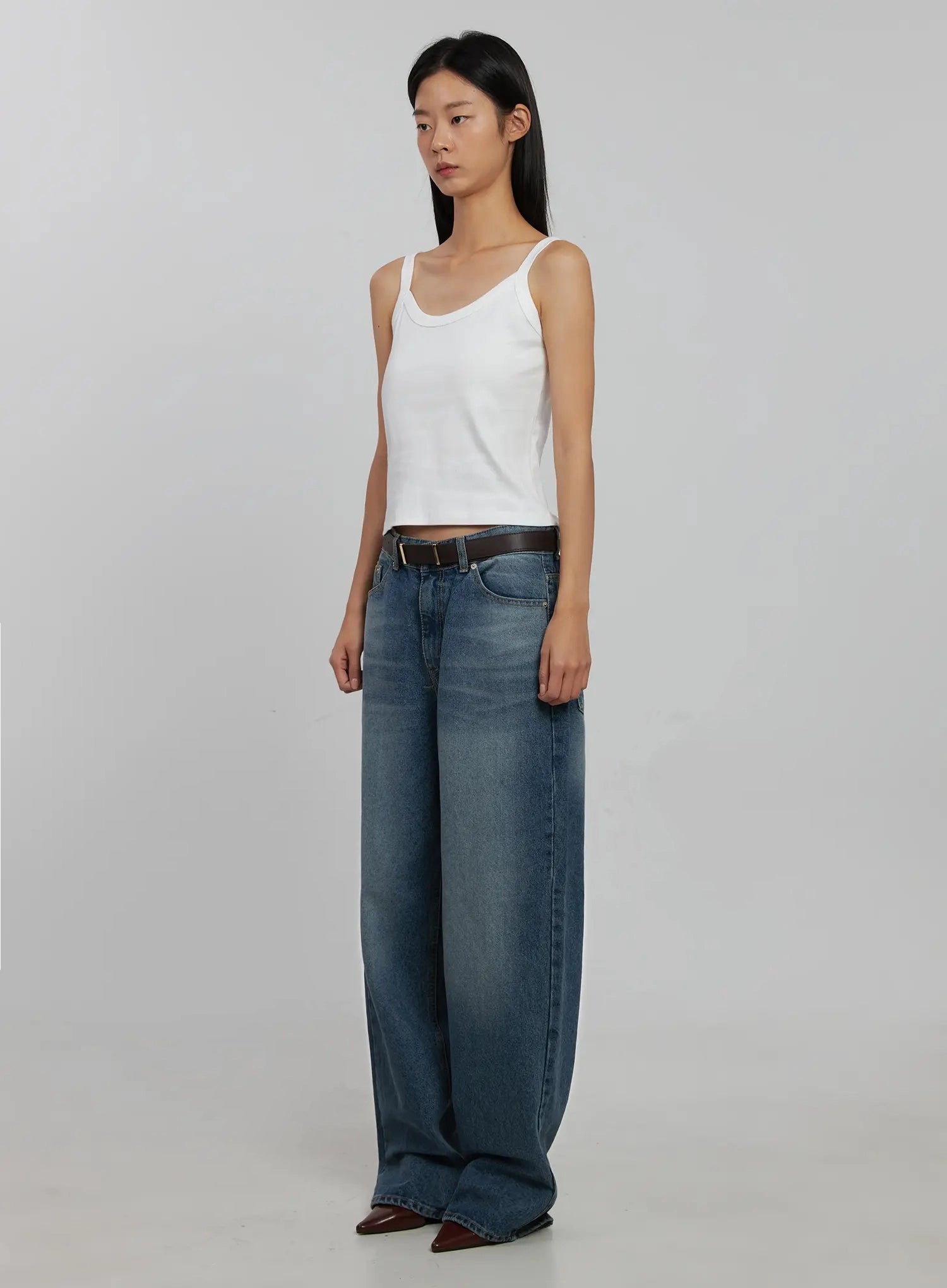 Akira Wide Leg Jeans IJ508 in blue, three-quarter front angle on model, wide-leg washed cotton silhouette, belted low rise, with white cami and burgundy heeled boots.