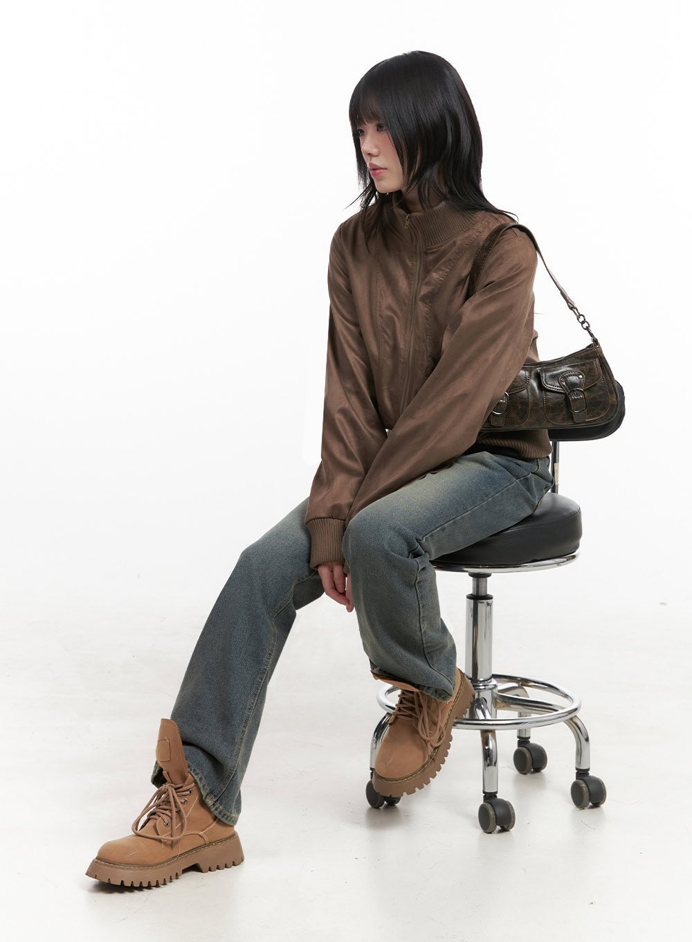 Asher Slimline Washed Bootcut Jeans ID402 in vintage blue, seated editorial shot on model atop stool, slim bootcut leg shown relaxed, styled with brown bomber jacket and tan lace-up boots.