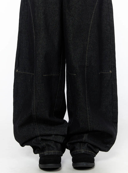 Lova Baggy Jeans CU519 in black, lower-leg detail close-up showing deep curved panel seams, contrast stitching, and gathered stacked hem over black shoes.