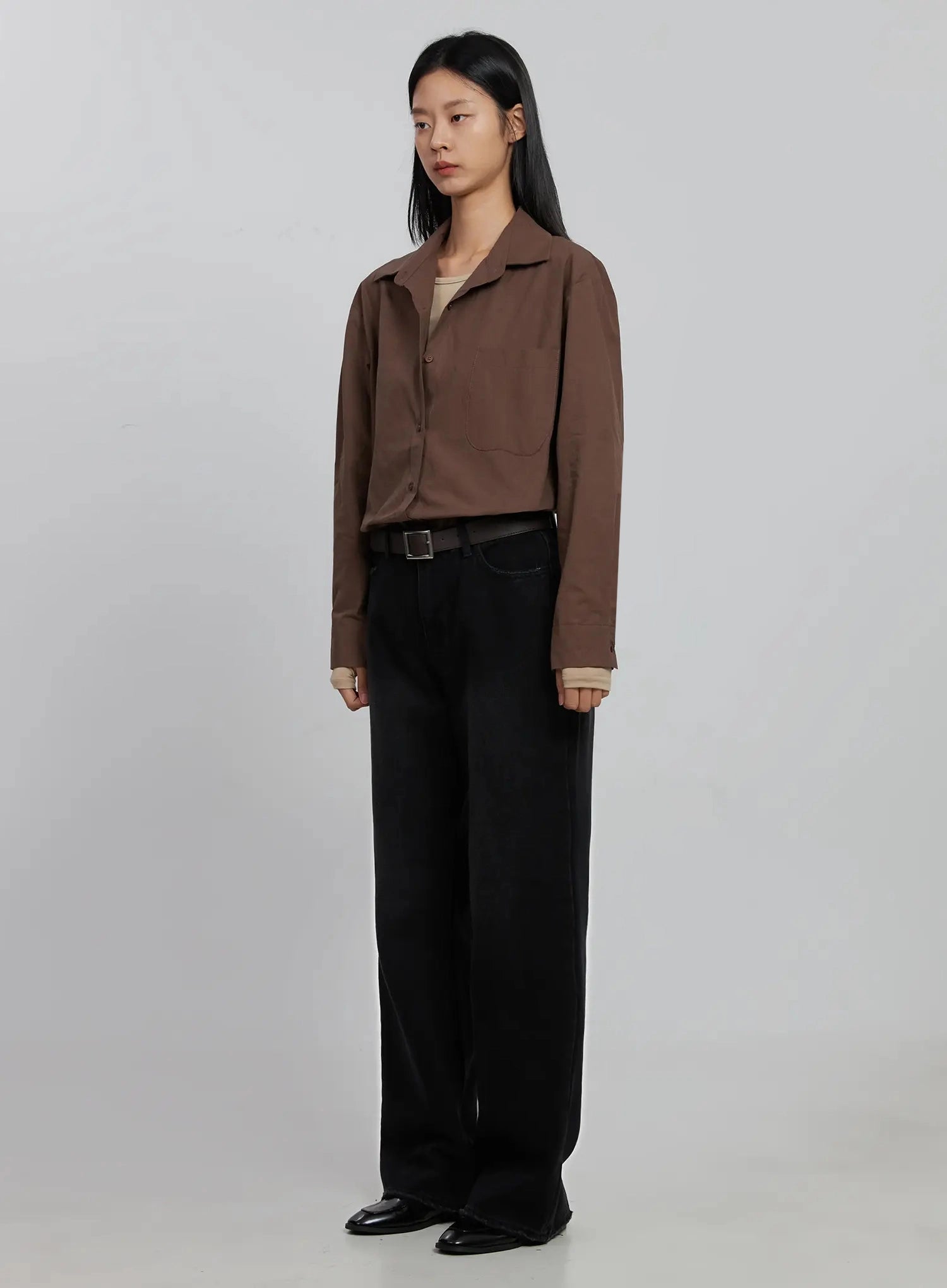 Imani Wide-Leg Flared Jeans ID516 in black, three-quarter front angle on model, paired with brown cropped shirt and beige inner top, dark belt, wide flared leg, long cotton denim, black loafers.