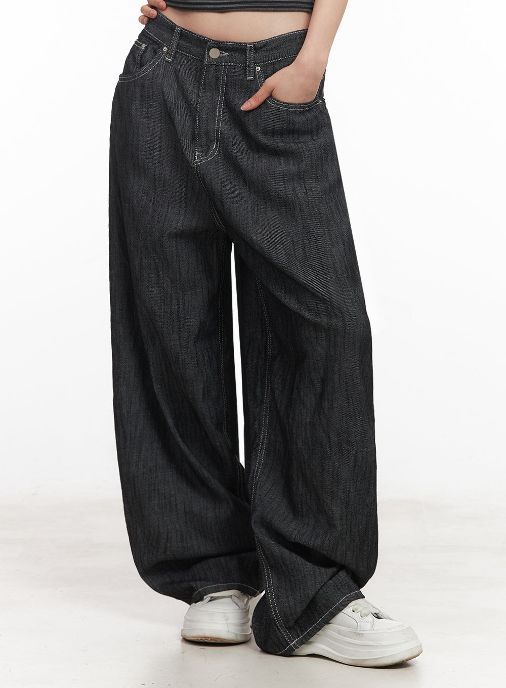 Lilli Wide-Leg Baggy Jeans IY516 in Black, side-front close-up on model, hand in pocket, wide denim fabric with visible contrast stitching and curved seam, white sneakers at hem.