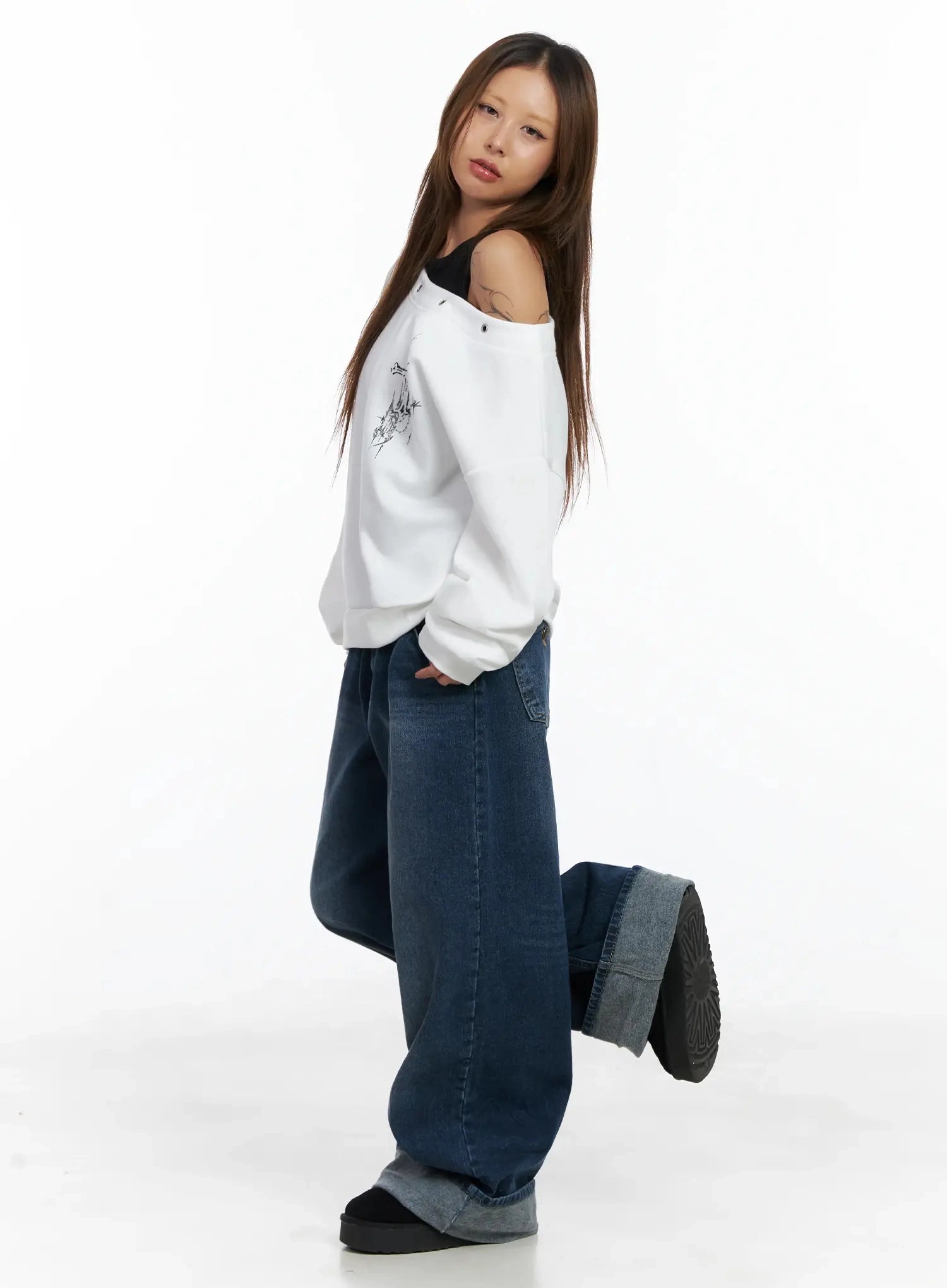 Anahi Baggy Jeans IN528 in blue, side editorial shot on model in dynamic pose, wide baggy leg and thick cuff visible, styled with off-shoulder white sweatshirt.