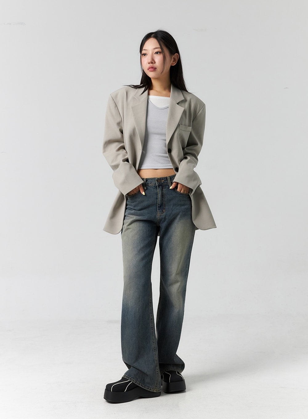 Vintage Wash Bootcut Jeans CS305 in blue, full-body slight side angle on model, hands in pockets, vintage wash denim with bootcut flare, styled with beige blazer and white crop top.