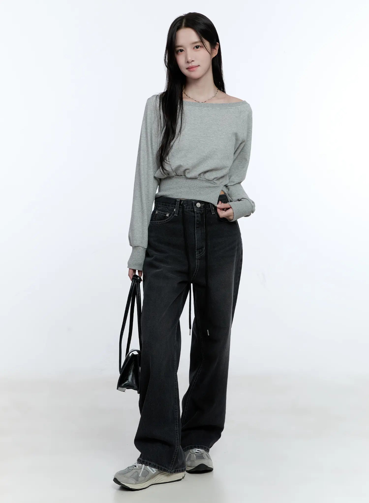 Lucinda High-Rise Wide Leg Jeans CG512 in black, full-body front shot on model holding black bag, washed high-rise wide leg denim with drawstring, styled with gray off-shoulder crop top and sneakers.