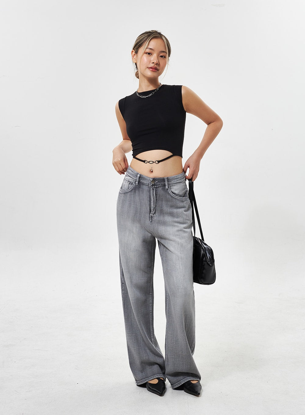 Mid-Rise Wide Leg Jeans CY330 in grey, full-length front shot on model adjusting waistband, wide-leg washed denim, styled with black crop top and shoulder bag.
