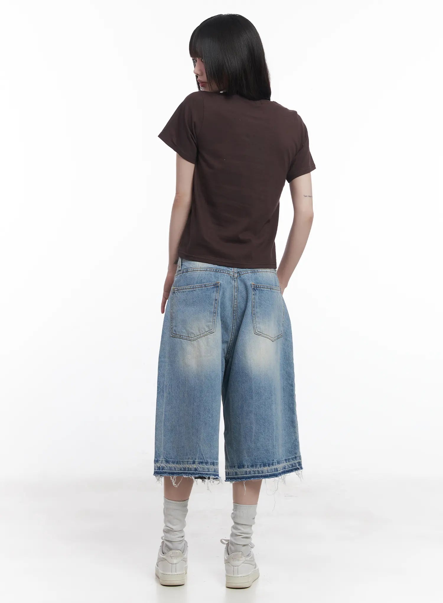 Light Wash Vintage Jorts CU519 in blue, back full-body on model, wide baggy silhouette with back patch pockets, vintage washed denim and raw frayed hem, paired with brown crop tee.
