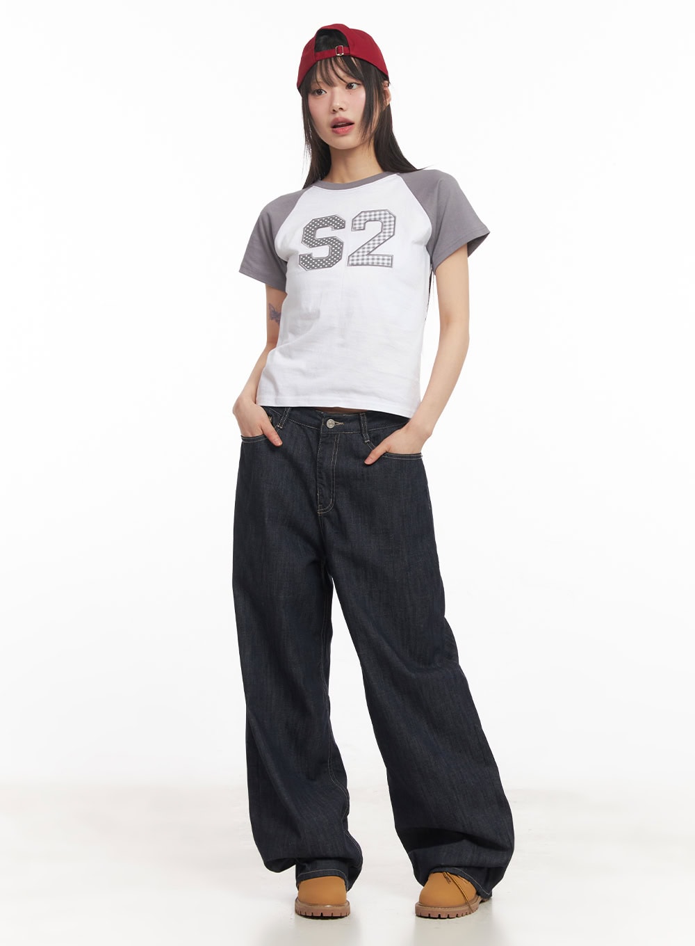 Ivara Wide-Leg Jeans CA522 in dark blue, front full-length view on standing model, low-rise wide-fit cotton denim, hands in pockets, styled with cropped raglan tee and red cap.