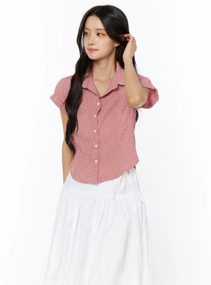 Gingham Button-Up Short Sleeve Blouse CU522 in red, angled front view on model with hand in hair, textured seersucker fabric and relaxed cropped hem, white skirt.