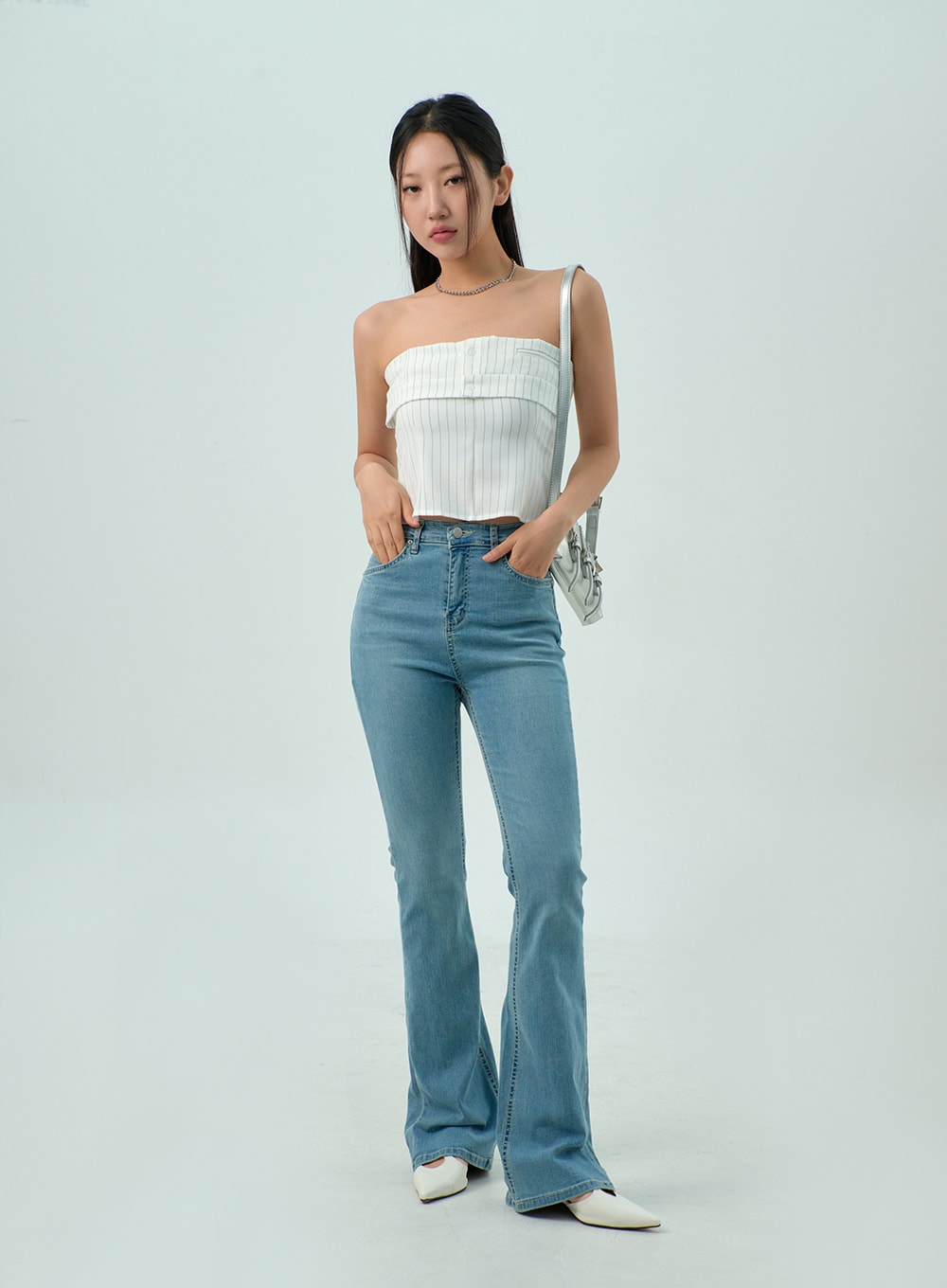 Light Wash Bootcut Jeans CY330 in light blue, full front view on model hand in pocket, high-rise slim-fit washed denim with bootcut flare, paired with white tube top and mini bag.