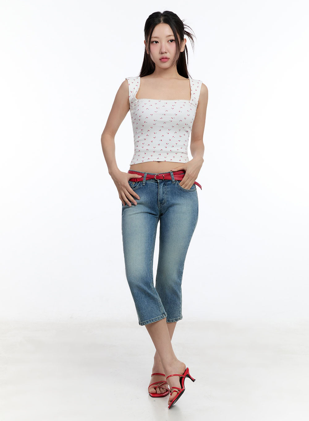 Kyra Cropped Low-Rise Skinny Jeans IU503 in blue, full-body front on model hands in pockets, washed skinny crop with red belt, styled with white cherry crop tank and red heeled sandals.