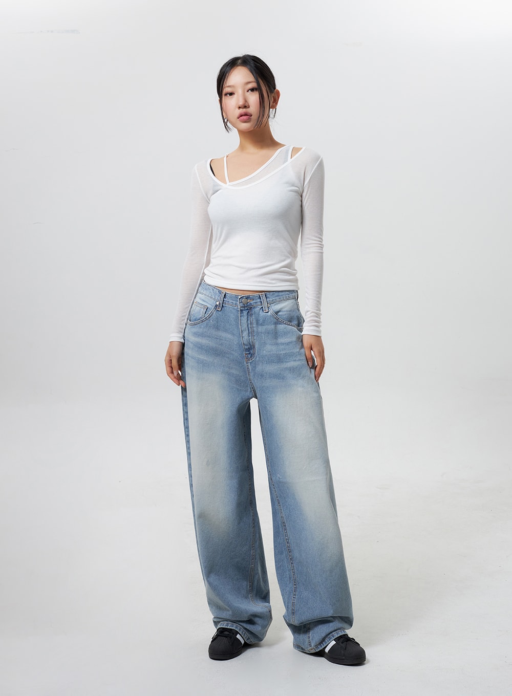 Low Rise Baggy Jeans CY324 in light blue, full-length front view on model standing relaxed, baggy wide-leg cotton denim with faded wash, paired with white cutout long-sleeve top and black sneakers.