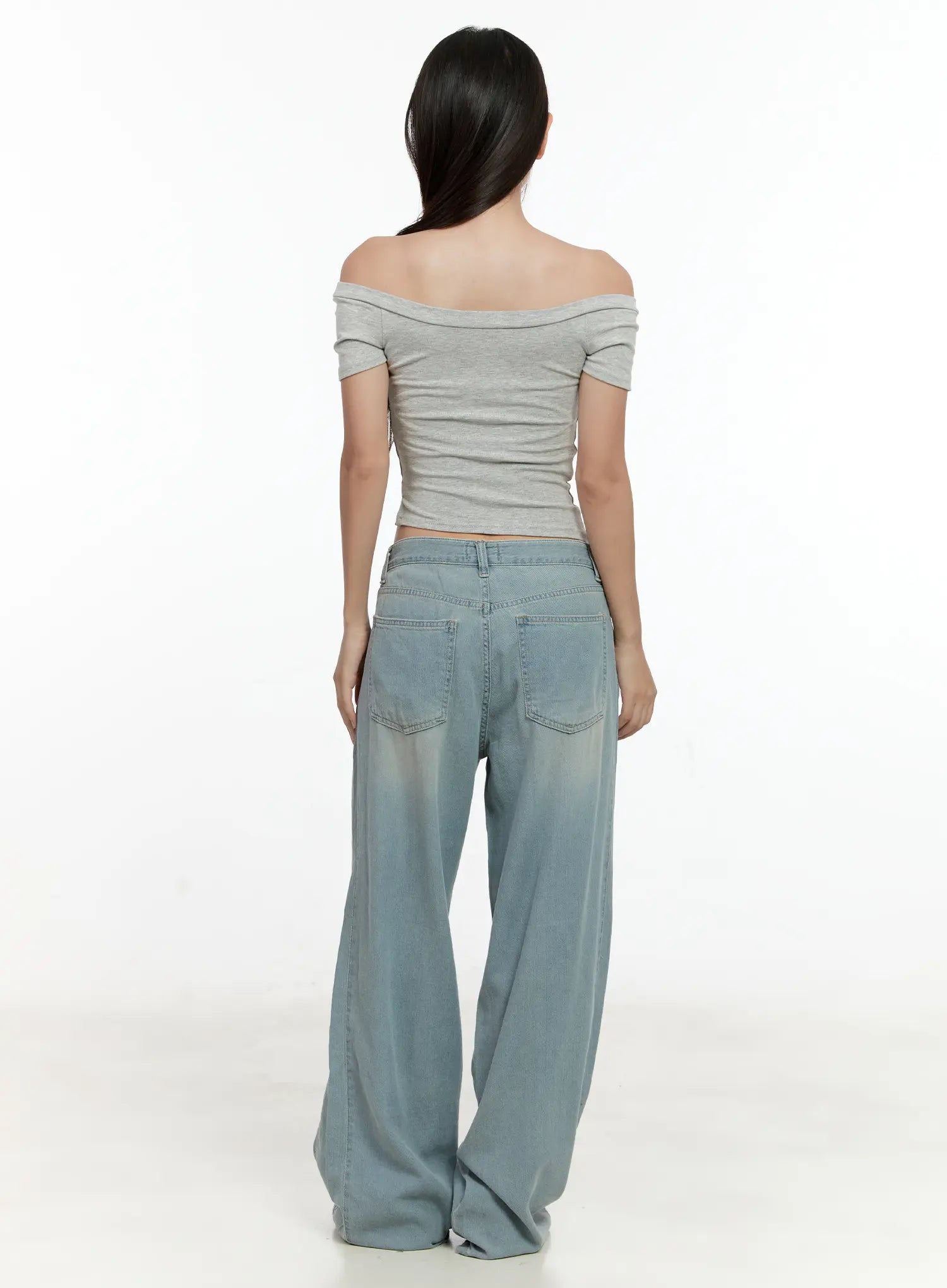 Huening Wide-Leg Jeans CL531 in blue, back view on model paired with grey off-shoulder crop top, washed low-rise wide-leg denim with back pockets and pooling hem at sneakers.