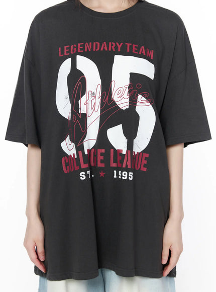 Oversized Graphic Tee CU519 in dark gray, graphic close-up on model torso, showing Legendary Team 95 Athletic College League distressed print detail with red and white lettering on crew neck tee.