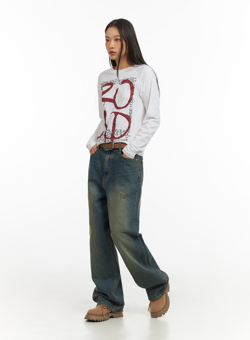 Anya Wide Fit Denim Jeans IO409 in blue, diagonal side-front pose on model, washed baggy denim with vintage green-yellow fade, distressed surface, paired with white graphic long-sleeve and brown belt.