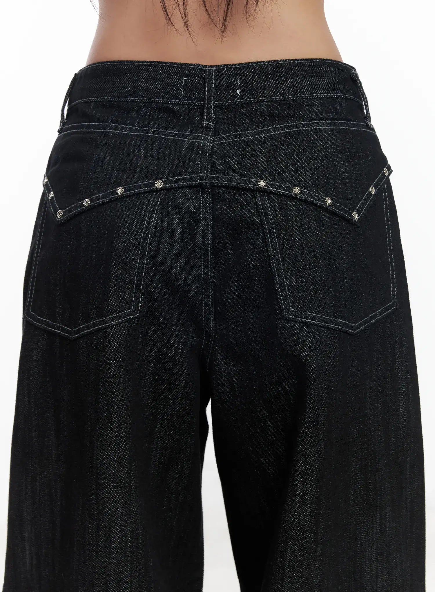 Violet Studded Baggy Jeans CJ530 in black, close-up back detail shot on model, silver floral stud trim along V-shaped back yoke, contrast white topstitching on patch pockets, raw denim texture.