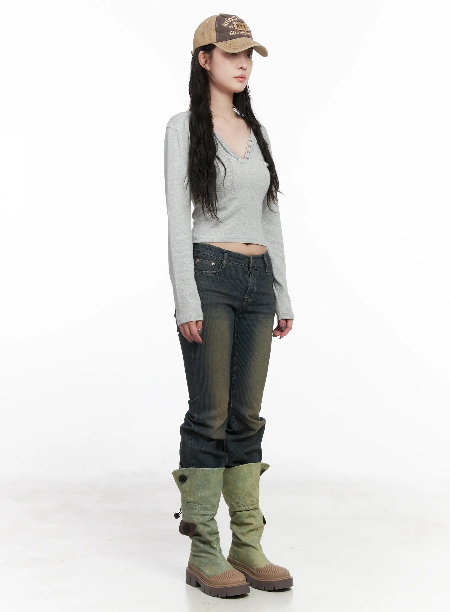Soleil Hip Pad Stripe Hip Pad Flared Jeans CN512 in dark blue, three-quarter front side editorial shot on model, washed stripe slim bootcut, low rise, styled with gray v-neck crop top, baseball cap, and green suede tall boots.
