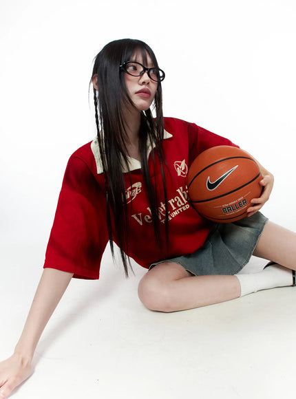 Oversized Collar Jersey CU519 in red, seated floor pose on model holding basketball, oversized sporty jersey with beige contrast collar and Velvet rabbit graphic, paired with denim mini skirt.