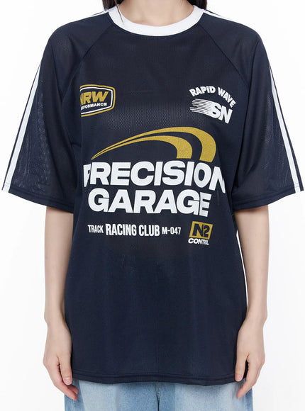 Oversized Sporty Graphic Tee CU519 in dark blue, front torso close-up on model, racing graphic detail with gold and white Precision Garage print, mesh fabric and white stripe sleeve visible.