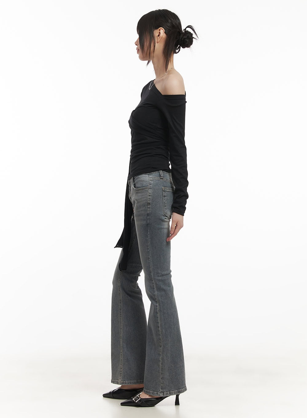 Rachel Washed Bootcut Jeans with Hip Pads CF518 in gray, side profile full-body shot on model, slim low-waist bootcut flare washed denim styled with black off-shoulder ruched top.