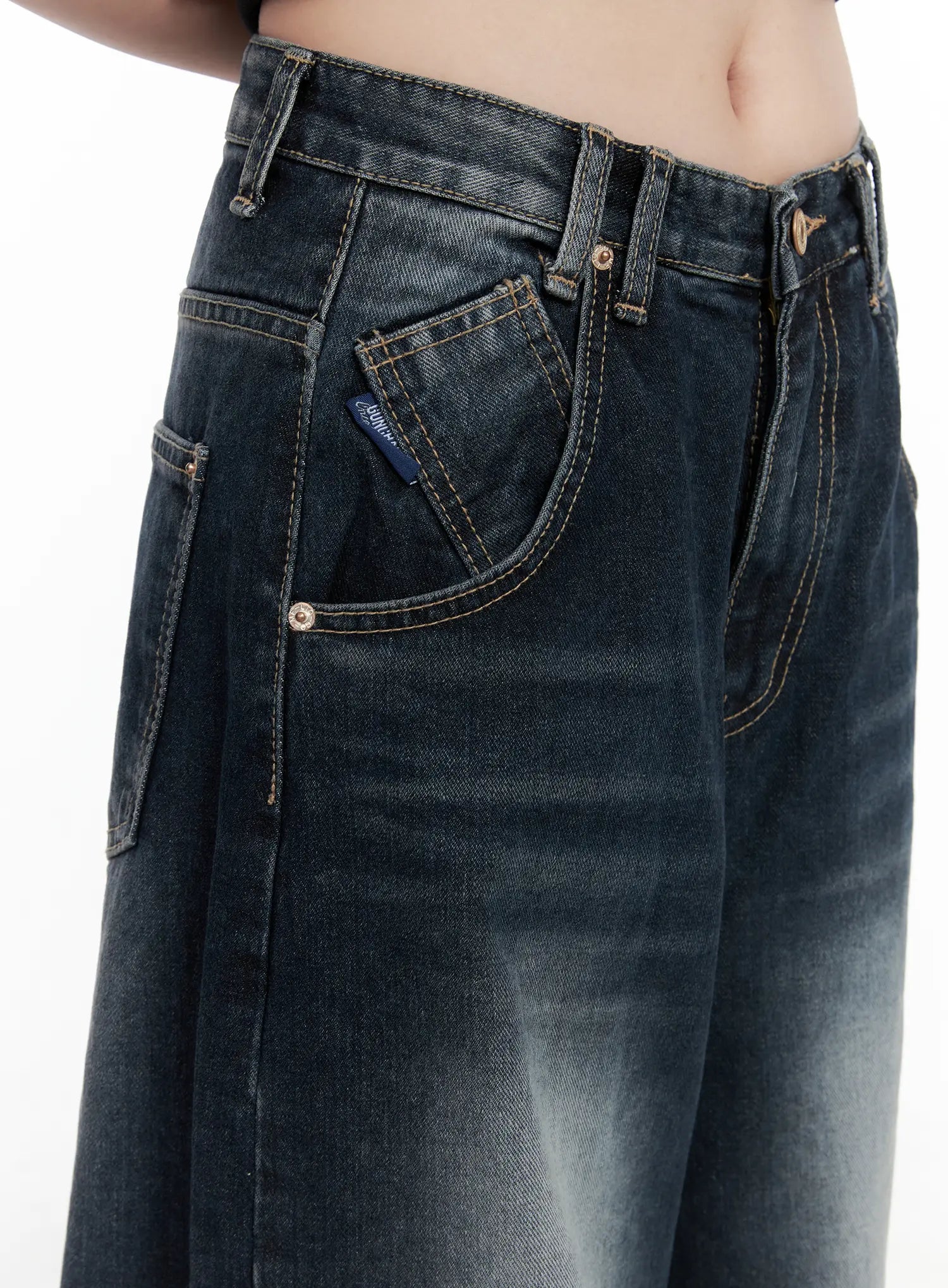 Isla Washed Baggy Jeans CO521 in dark blue, waist detail close-up on model, showing front pockets, LEWKIN woven label tab, gold rivets, and contrast topstitching on washed denim.
