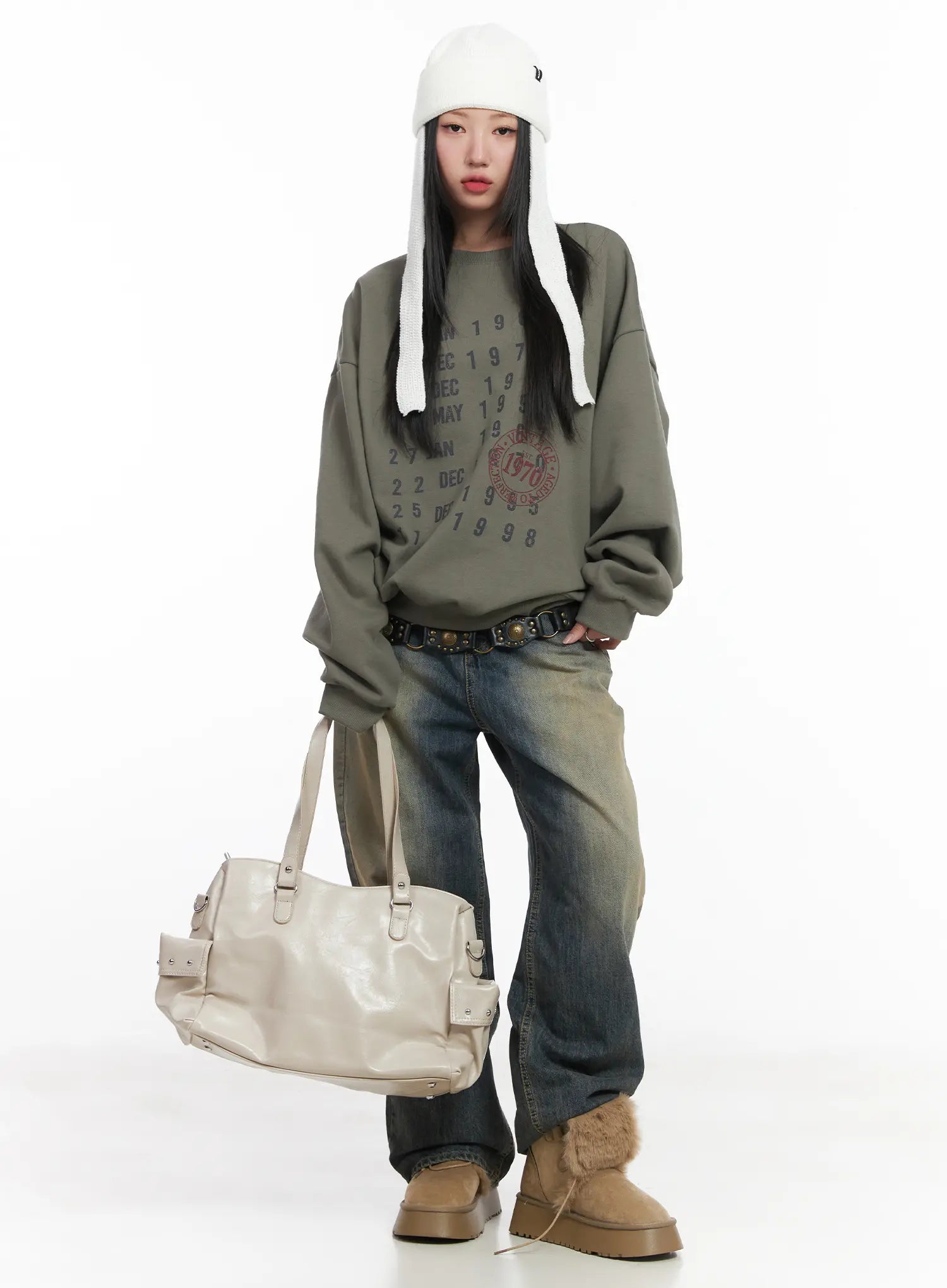 Wide Washed Jeans CS06 in vintage blue, full-length front editorial shot on model, wide-leg washed denim with belt, styled with olive graphic sweatshirt, cream shoulder bag, trapper hat, fur boots.