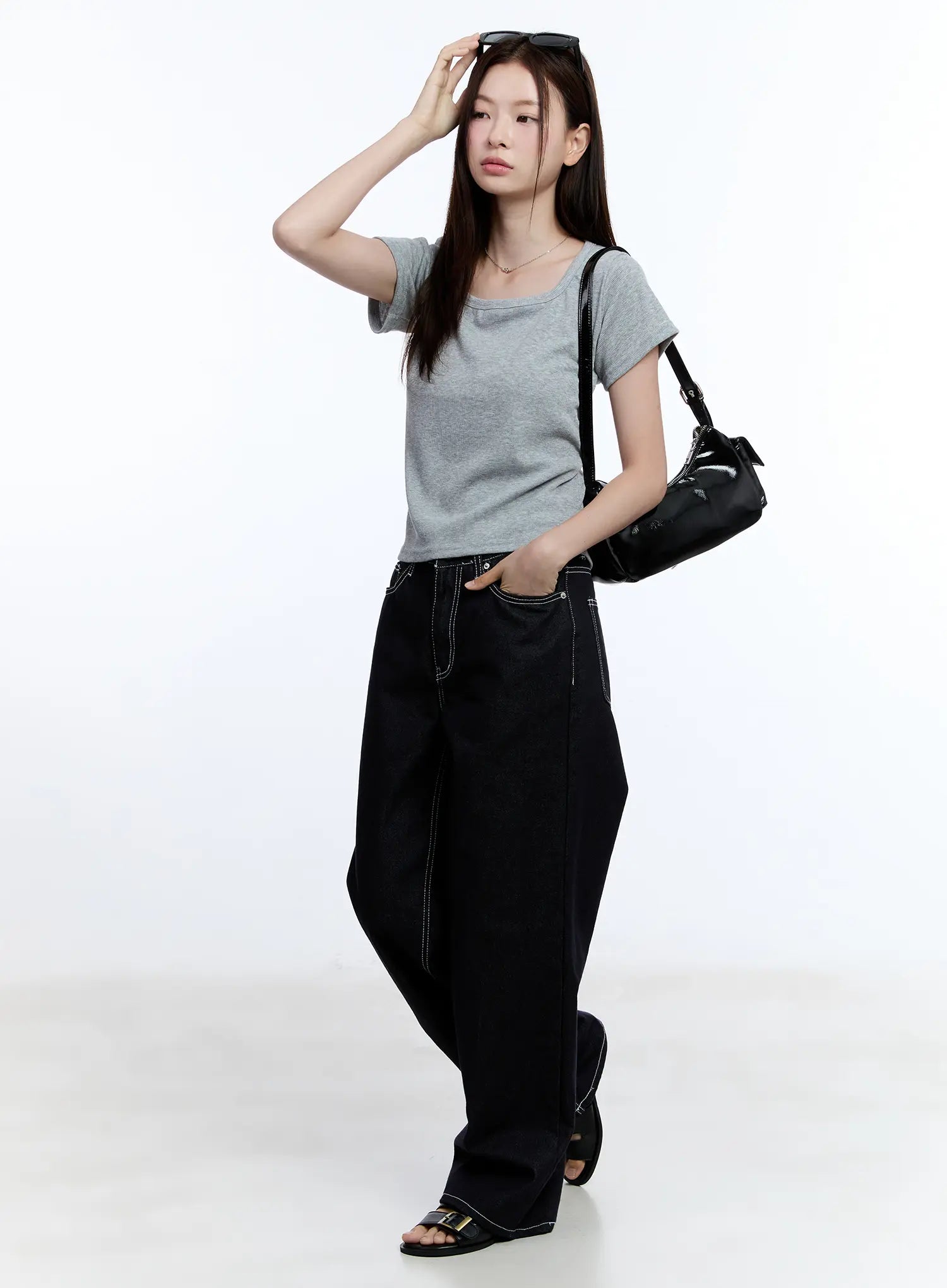 Nayeon No-Fade Denim Jeans CU513 in dark blue, full-body editorial shot on model with dynamic pose, wide-leg denim styled with grey tee, cylinder bag, sunglasses, and black sandals.
